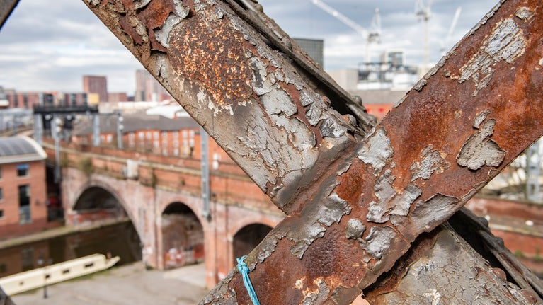 Looking through rusted steel lattice work towards a canal with a boat.